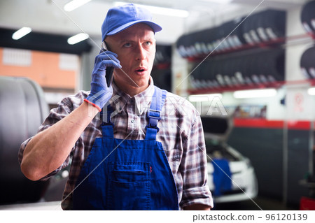 Confident auto mechanic talking on a smartphone in car service 96120139