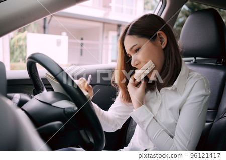 Woman working and eating at the wheel in the car, Busy woman is in a hurry. Woman working and eating at the wheel in the car, Busy woman is in a hurry. 96121417
