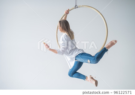 Caucasian female gymnast doing aerial hoop exercises and using smartphone.  96122571