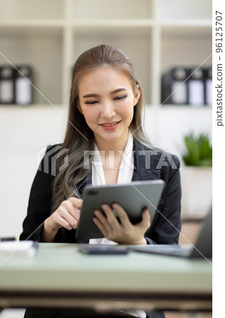 Professional Asian businesswoman reading something on her tablet, working in her office. Professional Asian businesswoman reading something on her tablet, working in her office. 96125707