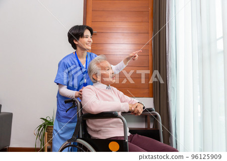 Friendly staff caregiver of nursing home talking to asian senior man in living room 96125909
