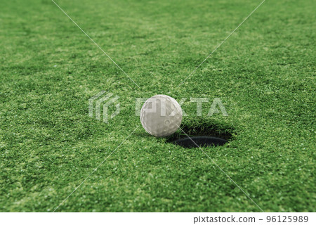Golf ball near the hole in a grass field Golf ball near the hole in a grass field 96125989