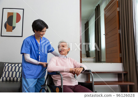 Friendly staff caregiver of nursing home talking to asian senior man in living room 96126028