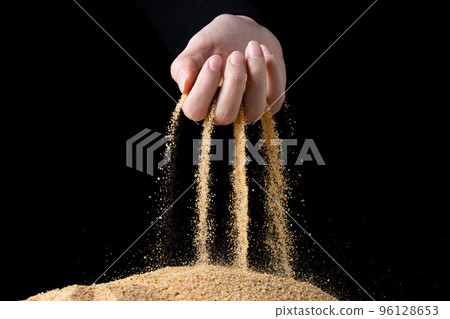 Hand releasing dropping sand. Fine Sand flowing pouring through fingers against black background. Summer beach holiday vacation and time passing concept. Isolated high speed shutter 96128653