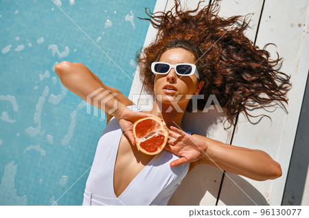 Beautiful woman in sunglasses rests near swimming pool Beautiful woman in sunglasses rests near swimming pool 96130077