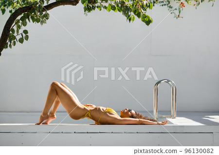 Beautiful woman enjoying suntan near private swimming pool 96130082