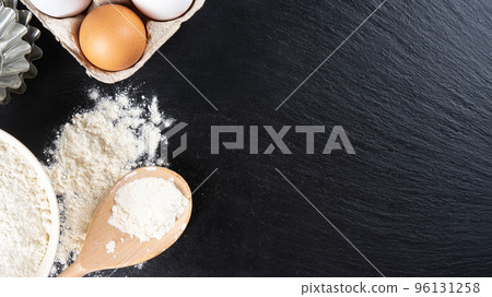 Baking ingredients flour, eggs, milk, bakeware on black slate background with copy space Baking ingredients flour, eggs, milk, bakeware on black slate background with copy space 96131258