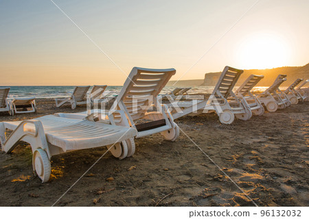 White sunbeds in a sandy beach at sunset 96132032