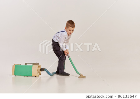 Portrait of cheerful little boy cleaning house with vacuum cleaner isolated over grey background Portrait of cheerful little boy cleaning house with vacuum cleaner isolated over grey background 96133647