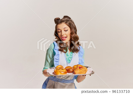 Portrait of stylish young woman, housewife with freshly baked buns isolated over grey background 96133710