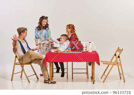 Portrait of beautiful young family sitting at the table and having breakfast together over grey background. Freshly baked buns 96133728
