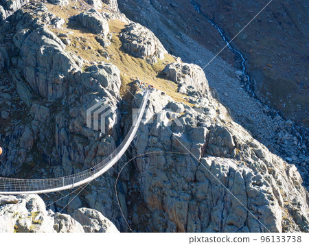 Trift, Switzerland - October 18th 2022: Spectacular rope bridge Triftbruecke crossing a canyon Trift, Switzerland - October 18th 2022: Spectacular rope bridge Triftbruecke crossing a canyon 96133738