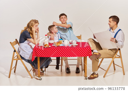 Portrait of lovely young family, woman, man and two boys sitting at the table and having breakfast isolated over grey background 96133778