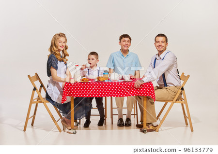 Portrait of lovely young family, woman, man and two boys sitting at the table and having breakfast isolated over grey background 96133779