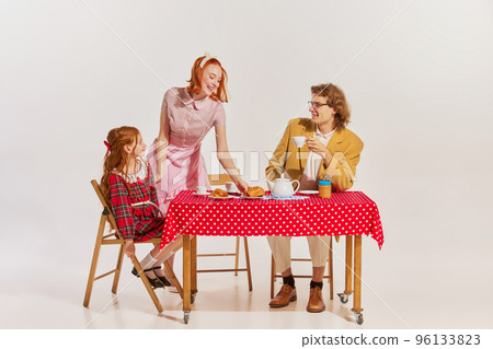 Portrait of beautiful woman, man and little girl sitting at the table and having breakfast isolated over grey background Portrait of beautiful woman, man and little girl sitting at the table and having breakfast isolated over grey background 96133823