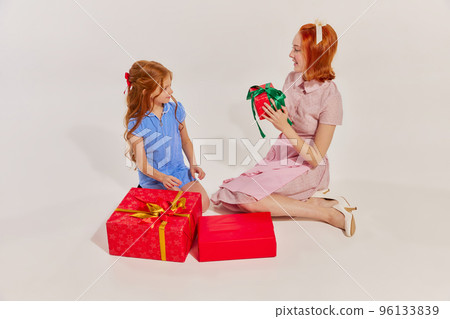 Portrait of beautiful woman, mother giving present to her daughter isolated over grey studio background. Winter holidays Portrait of beautiful woman, mother giving present to her daughter isolated over grey studio background. Winter holidays 96133839