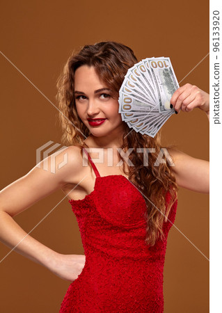 Image of lucky happy woman with brown long hair with fan of 100 dollar bills, lots of cash money, over brown background 96133920