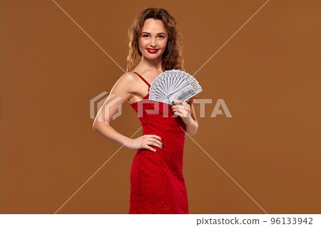 Blond curly woman weared in a red sexy dress is holding some hundred dollar bills in her hands. Casino. Blond curly woman weared in a red sexy dress is holding some hundred dollar bills in her hands. Casino. 96133942