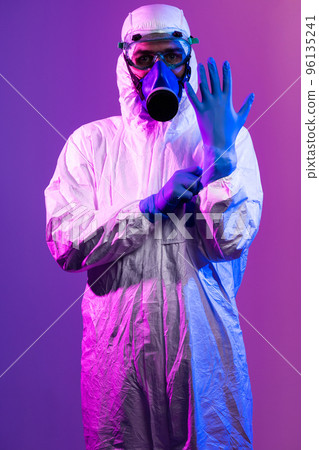 Coronavirus covid-19 pandemic. Doctor scientist wearing protective biological suit and mask due to global healthcare epidemic warning and danger background in blue and pink neon lights background. 96135241