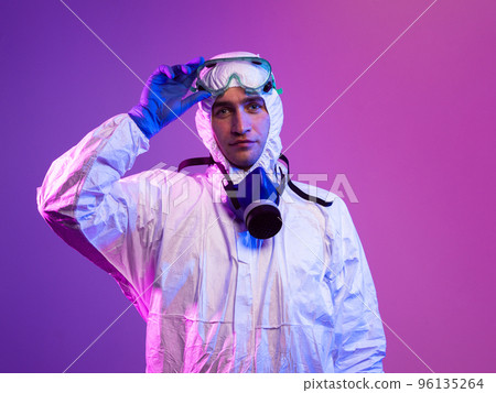 Coronavirus covid-19 pandemic. Doctor scientist wearing protective biological suit and mask due to global healthcare epidemic warning and danger background in blue and pink neon lights background. Coronavirus covid-19 pandemic. Doctor scientist wearing protective biological suit and mask due to global healthcare epidemic warning and danger background in blue and pink neon lights background. 96135264