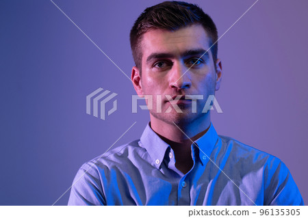 A man in a shirt poses on a dark multicolored neon background A man in a shirt poses on a dark multicolored neon background 96135305