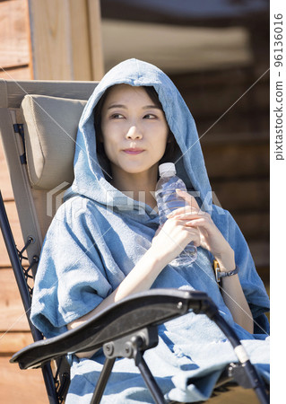 Sauna girls wearing a sauna poncho and taking an open air bath in front of an outdoor sauna 96136016