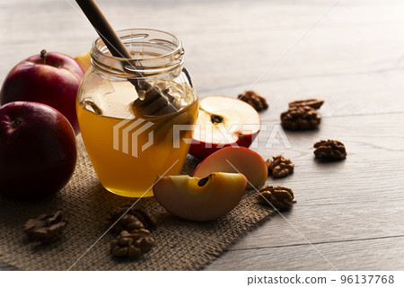 Mason jar with honey honey dipper red apples and walnuts on kitchen table 96137768