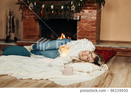A charming young woman lies on a rug by the fireplace on Christmas Eve A charming young woman lies on a rug by the fireplace on Christmas Eve 96139930