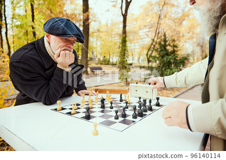 Portrait of senior man playing chess in the park on a daytime in fall. Concept of leisure activity, old generation Portrait of senior man playing chess in the park on a daytime in fall. Concept of leisure activity, old generation 96140114