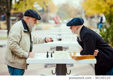 Portrait of two senior men playing chess in the park on a daytime in fall. Warm day walk. Concept of leisure activity, old generation 96140120