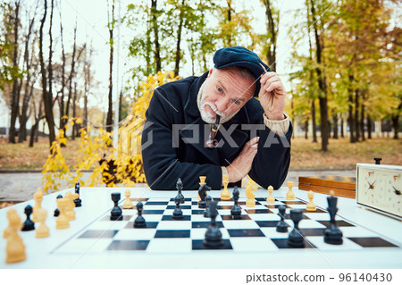 Portrait of senior bearded man playing chess and smoking pipe in the park on a daytime in fall. Thoughtful look. Concept of leisure activity, old generation 96140430