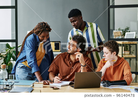 Happy young businessman looking at colleague pointing at his notes in copybook during explanation of working points among coworkers 96140478