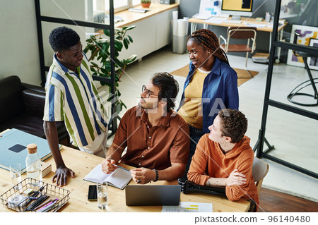 Group of four intercultural managers or creative designers having discussion of their ideas and working strategies at meeting 96140480
