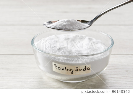 Close-up of baking soda on spoon against background of bowl on wooden table. 96140543