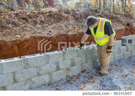 Man levels tool during construction of concrete block retaining wall on new property that is being built Man levels tool during construction of concrete block retaining wall on new property that is being built 96141607