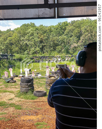 Man firing pistol at target in outdoor shooting range 96141957