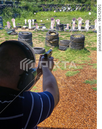 Man firing pistol at target in outdoor shooting range 96142001
