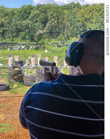 Man firing pistol at target in outdoor shooting range 96142031
