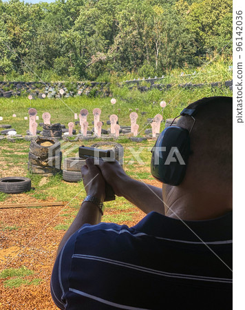 Man firing pistol at target in outdoor shooting range 96142036