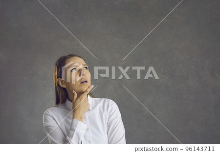 Woman with a pensive expression standing on a gray background thinking about a solution. Woman with a pensive expression standing on a gray background thinking about a solution. 96143711