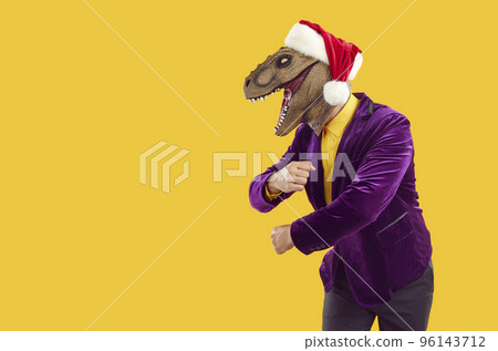Funny man in dinosaur mask, Christmas hat and party suit dancing on copy space background Funny man in dinosaur mask, Christmas hat and party suit dancing on copy space background 96143712