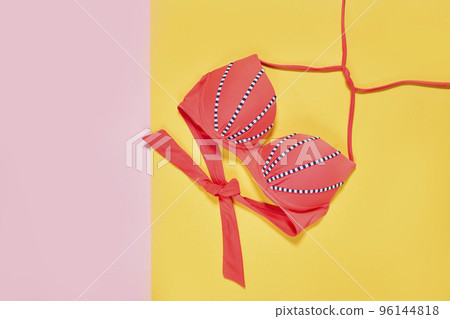 two pink and blue bikinis on a yellow background, with the one in black and white striped fabric tied around it 96144818