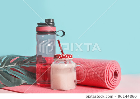 a water bottle and towel on a table next to a glass jar with a straw in it, surrounded by green leaves a water bottle and towel on a table next to a glass jar with a straw in it, surrounded by green leaves 96144860