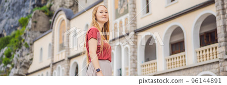 BANNER, LONG FORMAT Woman tourist in Monastery of Ostrog, Serbian Orthodox Church situated against a vertical background, high up in the large rock of Ostroska Greda, Montenegro. Dedicated to Saint 96144891