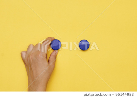 a person's hand holding two blue buttons on a yellow background, with the other one pointing towards them a person's hand holding two blue buttons on a yellow background, with the other one pointing towards them 96144988