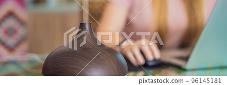 Essential oil diffuser on the table steaming while woman using laptop BANNER, LONG FORMAT 96145181