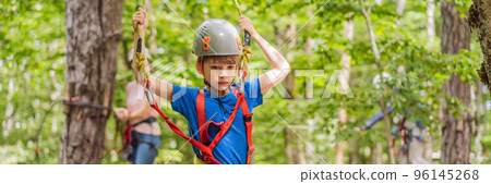 BANNER, LONG FORMAT Mother and son climbing in extreme road trolley zipline in forest on carabiner safety link on tree to tree top rope adventure park. Family weekend children kids activities concept 96145268
