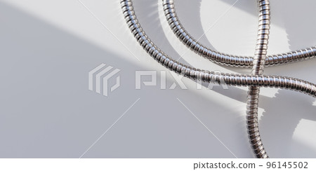 Metal shower hose on white background. Flexible chrome tube. Corrugated plumbing tube on banner with copy space on hard sunlight and shadow. 96145502