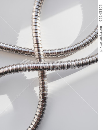 Metal shower hose on white background. Flexible chrome tube. Corrugated plumbing tube on geometrical banner with copy space on hard sunlight and shadow. 96145503