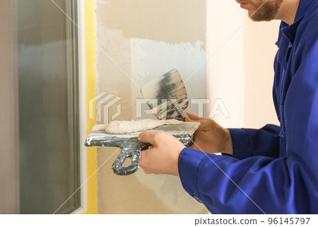 Professional worker with putty knifes and plaster near window indoors, closeup. Interior repair 96145797